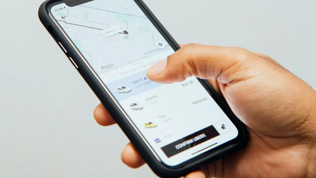 A person holds a mobile phone displaying a ride-hailing app with sleek UX and UI design in mobile app, showing a map and ride options like UberX, UberXL, and Taxi. Their thumb hovers near the CONFIRM UBERX button.